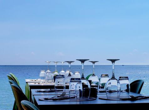 Elegant Served Restaurant Tables with Various Stemware and Silverware on Terrace in Shadow on Sea Coast Outdoors