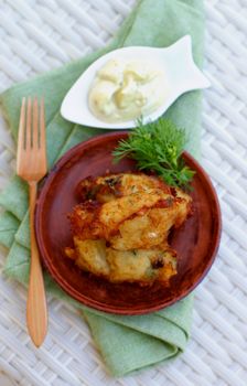 Top View of Delicious Breaded Fish Cutlets with Garlic, Greens and Tartar Sauce on Brown Plate with Wooden Fork on Wicker background. Focus on Fish