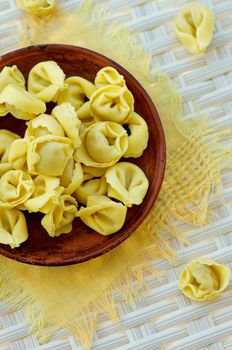 Raw Meat Cappelletti on Brown Plate with Yellow Napkin closeup on Wicker background. Top View