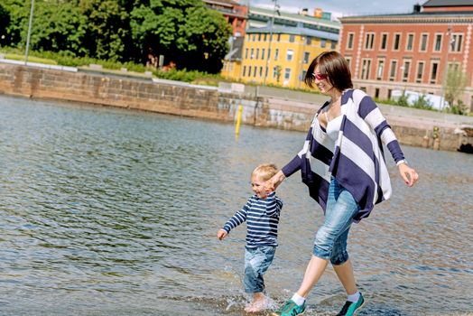 Little preschool boy playing on shore outdoors with brunette mother