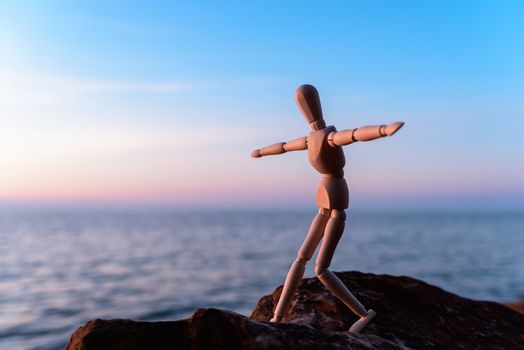 Wooden man stands on the top of sea boulder