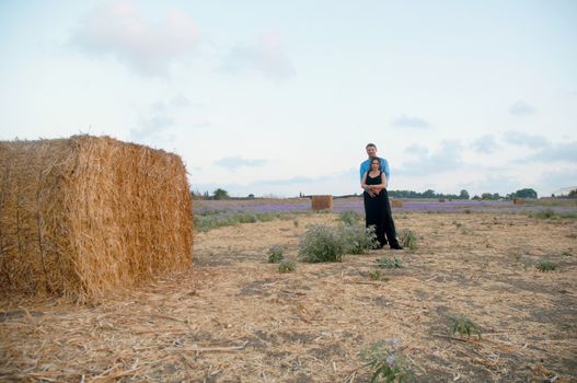 Elegant young couple on a romantic walk in a field of blossoming lavender and oblique hay.