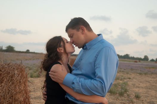 Elegant young couple on a romantic walk in a field of blossoming lavender and oblique hay.