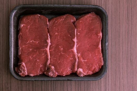 Three raw steaks into a black dish