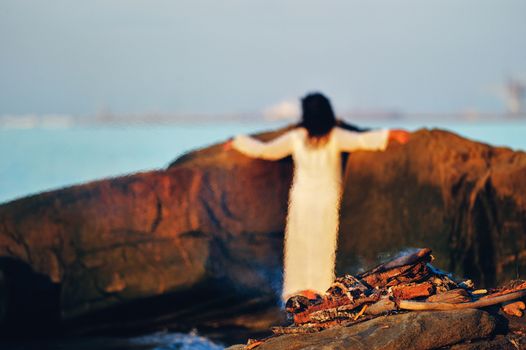 Woman in white dress near the campfire on the coast