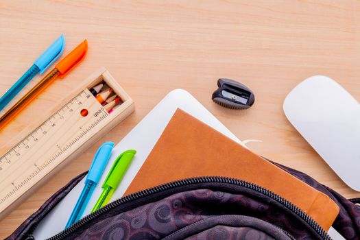 Backpack with school supplies laptop,book stationary,mouse,pen,ruler, and color pencil on wooden table .