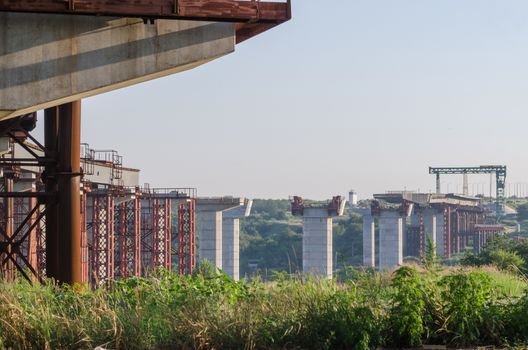 the construction of a bridge across the river with the supports, structural elements, cranes