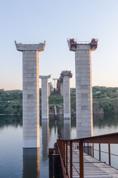 the construction of a bridge across the river with the supports, structural elements, cranes