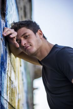 Attractive young man standing leaning against colorful graffiti wall, looking at camera