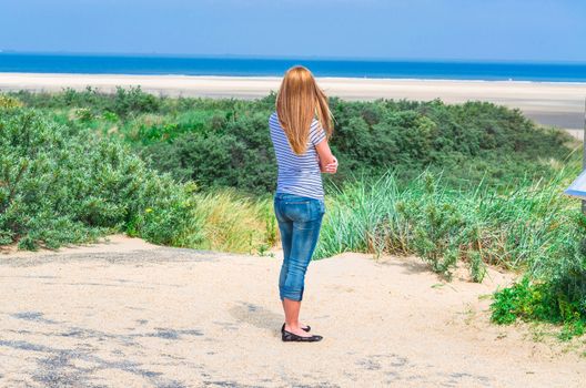 Young woman in summer with jeans standing on the beach with views of the sea. Girls relax and enjoy tranquility in the holiday.
