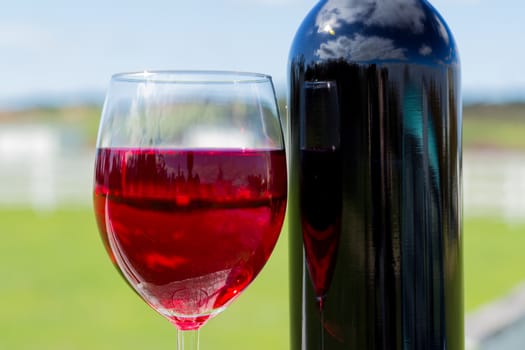 A glasss of red wine and a bottle of wine with a blurred background.