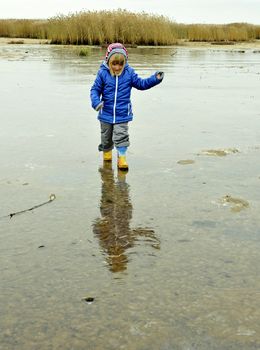 The little girl goes on the sandy coast in winter clothes