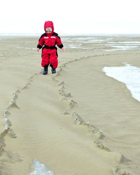 The little girl goes on the sandy coast in winter clothes