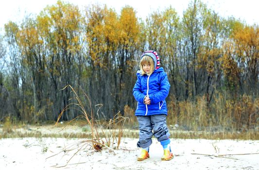 The little girl goes on the sandy coast in winter clothes