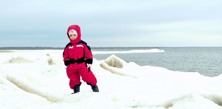 little girl in winter clothes on the snow-covered coast