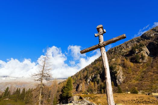 Old wooden cross (trunks of trees) tied with ropes with blue sky and clouds in the National Park of Adamello Brenta. Trentino Alto Adige, Italy