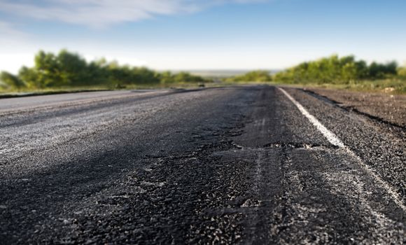 bad asphalt road through the green field and blue sky in summer day