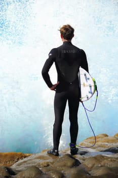 CAPE SOLANDER, AUSTRALIA - 9 AUGUST, 2015; Large waves splashes up against a surfer.  He is wearing a wetsuit and holding his surf board.