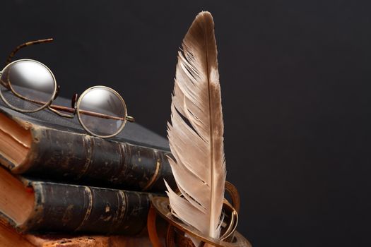 Vintage still life with quill pen near book and spectacles on dark background