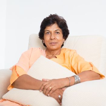 Portrait of a tired 50s Indian mature woman resting on sofa at home. Indoor senior people living lifestyle.