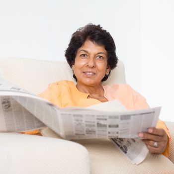 Portrait of a 50s Indian mature woman reading newspaper at home. Indoor senior people living lifestyle.