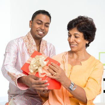 Portrait of happy Indian family celebrate birthday at home. Mature 50s Indian mother received surprised present from her 30s grown son.