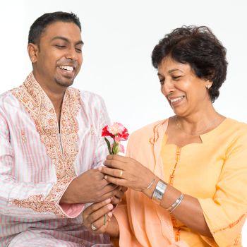 Portrait of happy Indian family celebrate mothers day at home. Mature 50s Indian mother received flower from 30s grown son.