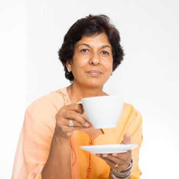 Portrait of a 50s Indian mature woman drinking coffee at home. Indoor senior people living lifestyle.