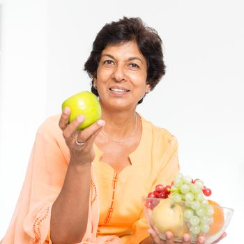 Old people healthy eating. Portrait of a 50s Indian mature woman eating fruits at home. Indoor senior people living lifestyle.