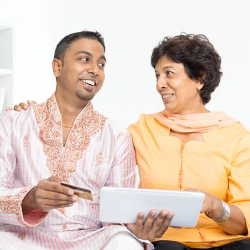 Portrait of Indian family using internet payment at home. Mature 50s Indian woman and 30s grown son happy online shopping with credit card.