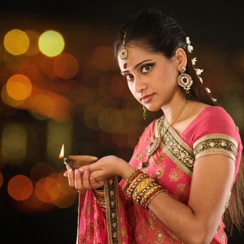 Indian girl in traditional sari lighting oil lamp and celebrating Diwali or deepavali, fesitval of lights at temple. Female hands holding oil lamp, beautiful lights bokeh background.