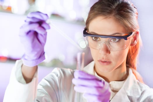 Life scientists researching in laboratory. Focused female life science professional pipetting solution into the glass cuvette. Lens focus on researcher's eyes. Healthcare and biotechnology concept.