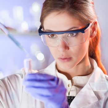 Life scientists researching in laboratory. Focused female life science professional pipetting solution into the glass cuvette. Lens focus on researcher's eyes. Healthcare and biotechnology concept.