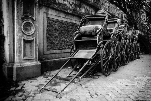 Black and white image of traditional hand pulled Indian rickshaws parked together in front of a old building in Kolkata