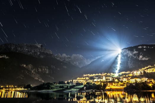 Night landscape on the Moveno lake and city with Dolomiti of Brenta Group in background at the moonlight and star trails