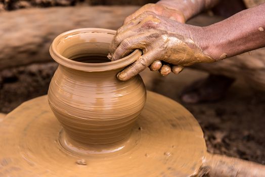 Closeup image of a potter's hands shaping soft clay to make an earthen pot