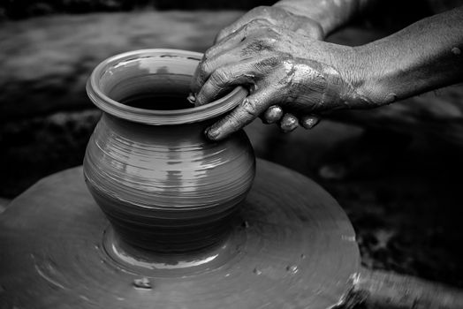 Black and white stricking image of a potter's hands shaping soft clay to make an earthen pot