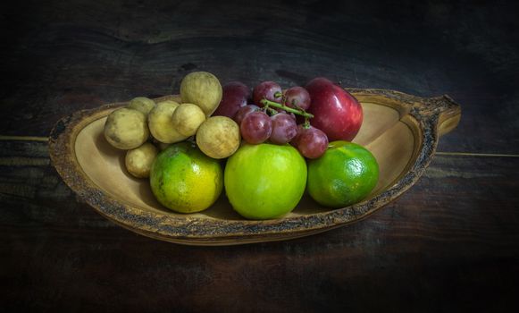 fruits in a wooden bowl on dark tone background