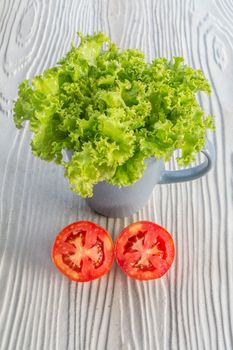 garnich lettuce in a grey mug, half cut tomato on wooden background