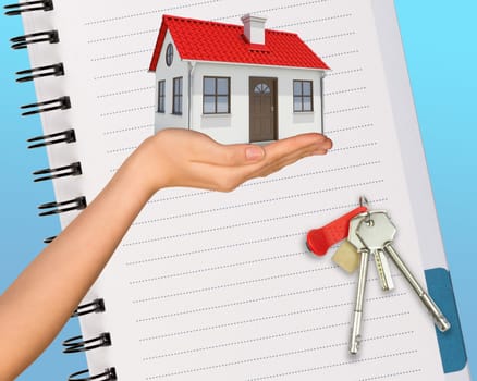 Humans hand holding house with keys and open notebook