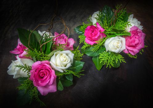 still life decorated pink and white roses with various leaves on dark tone wooden background