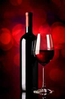 Bottle and glass with red wine on red background