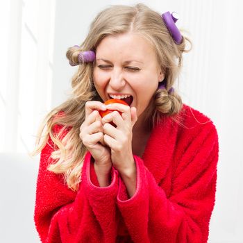 Girl in a red robe and curlers eating an apple