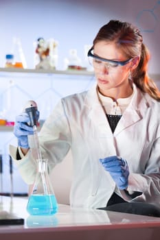 Life scientists researching in laboratory. Focused female life science professional pipetting blue solution into glass cuvette. Lens focus on researcher's eyes. Healthcare and biotechnology concept.