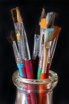 Muitiple paintbrushes in a dirty glass jar. 