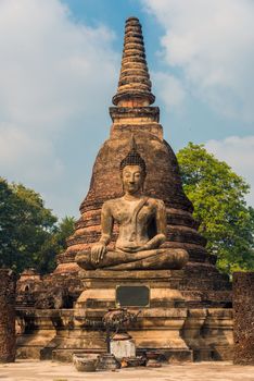 Large ancient statue of seated Buddha in front of a Stupa in Sukhothai, Thailand 