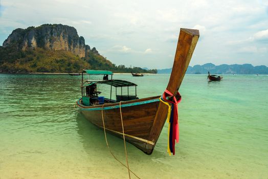 Longtail boat moored off a white sand Krabi beach in the crystal clear turquoise waters of Andaman sea.