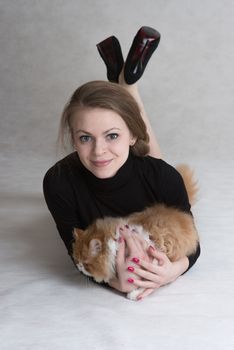 Very nice blonde lies on a floor and holds a red persian kitten