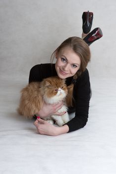 Very nice blonde lies on a floor and holds a red persian kitten