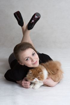 Very nice blonde lies on a floor and holds a red persian kitten